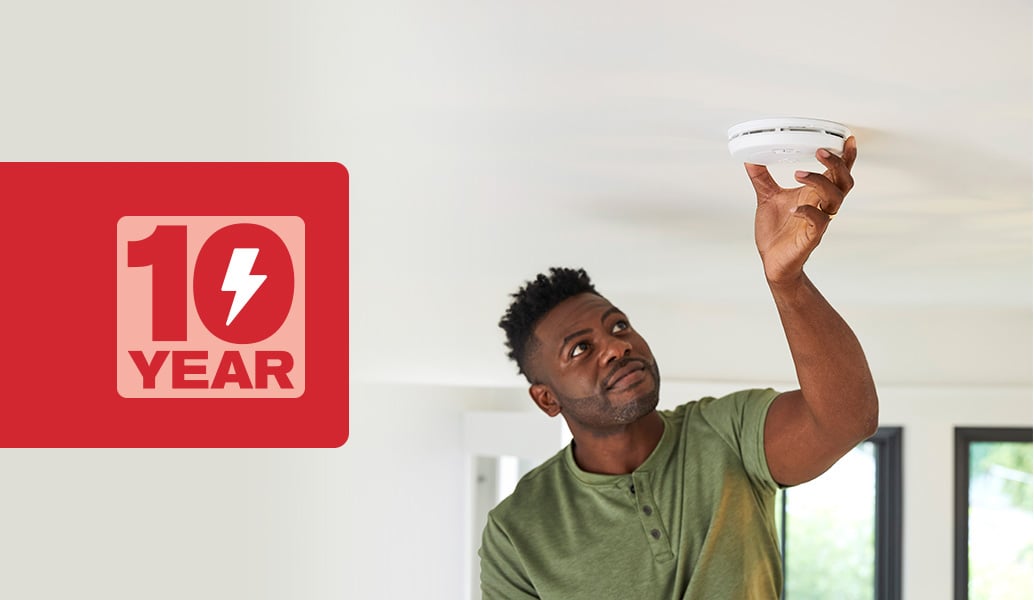 Man installing a First Alert 10-year battery smoke alarm on to his ceiling.