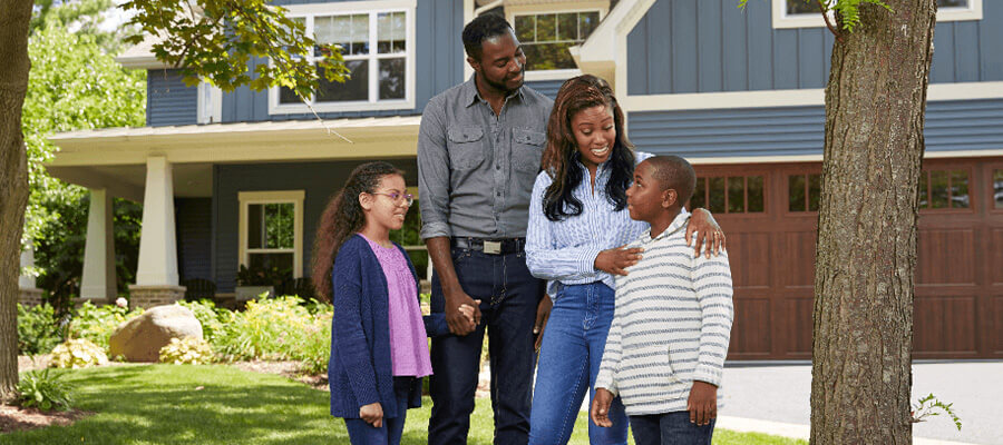 A father and mother stand outside their home with their young son and daughter.
