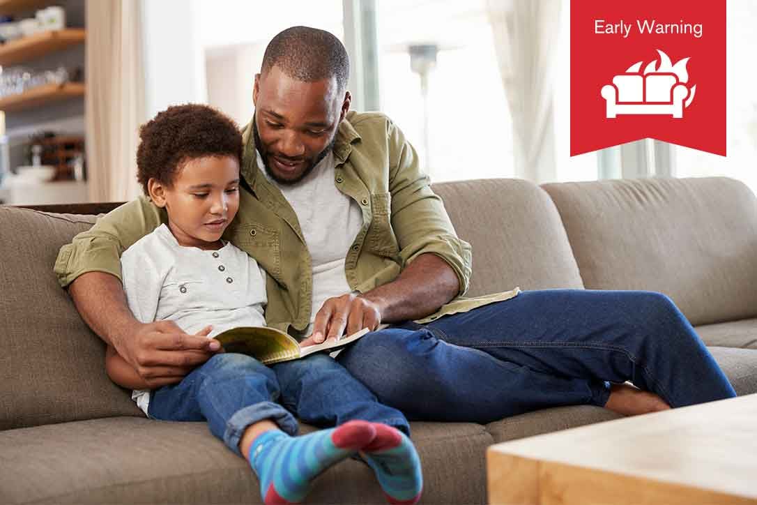 Early Warning. A man sits on a couch with his child as they read a book.